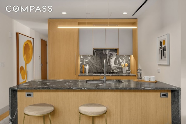 interior space with a breakfast bar area, white cabinetry, kitchen peninsula, dark stone counters, and decorative backsplash