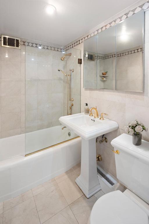 bathroom with toilet, tile walls, and tiled shower / bath