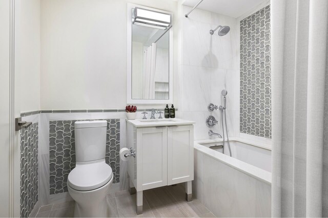 full bathroom with shower / bathtub combination, toilet, a wainscoted wall, vanity, and tile walls