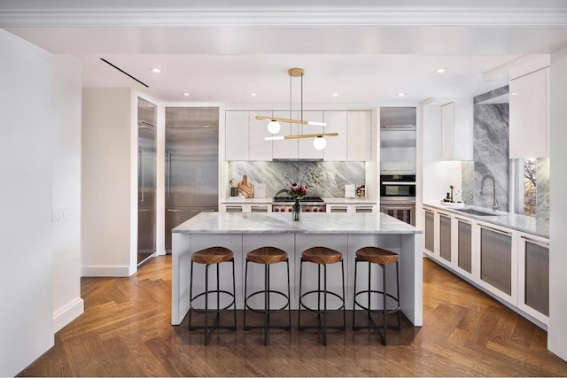 kitchen featuring hanging light fixtures, an island with sink, dark parquet flooring, and white cabinetry