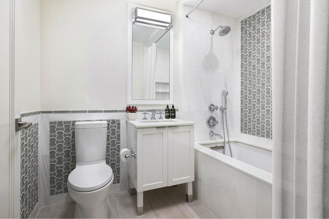 full bathroom with toilet, tile walls, vanity, and tiled shower / bath combo