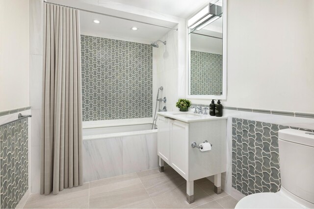 full bath featuring a wainscoted wall, tile walls, shower / bathtub combination, toilet, and tile patterned floors