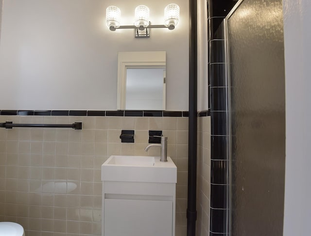 full bath featuring an enclosed shower, wainscoting, vanity, and tile walls