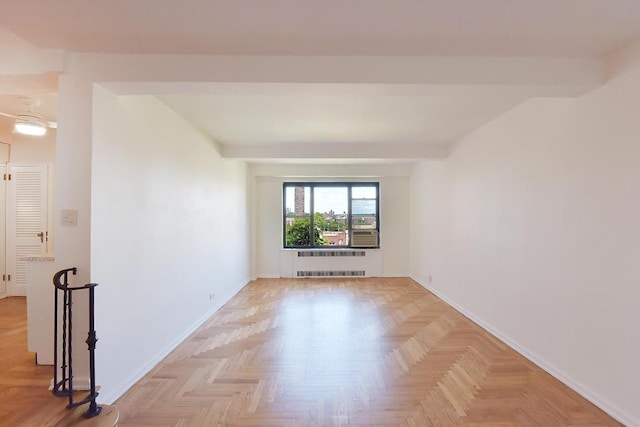 empty room with beam ceiling, light parquet floors, and radiator heating unit