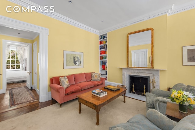 living area with built in shelves, wood finished floors, baseboards, a high end fireplace, and crown molding