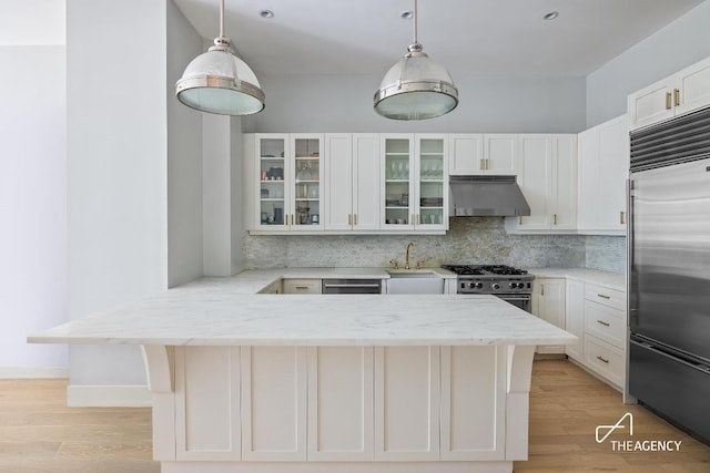 kitchen with light stone countertops, premium appliances, white cabinets, and hanging light fixtures