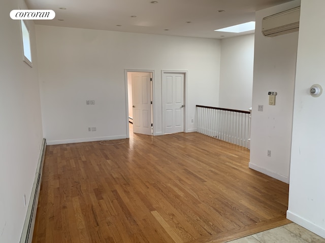 unfurnished room with light wood-type flooring, an AC wall unit, a skylight, and a baseboard heating unit