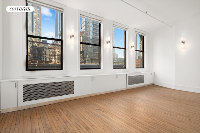 empty room featuring radiator, baseboards, and light wood finished floors