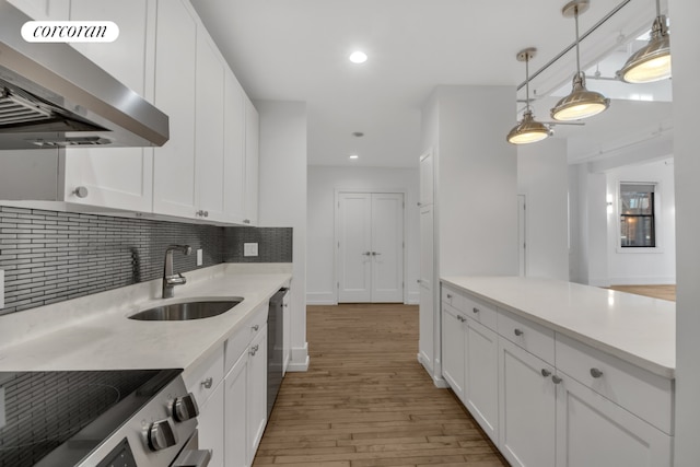 kitchen featuring appliances with stainless steel finishes, range hood, light countertops, white cabinetry, and a sink