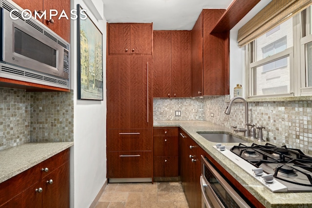 kitchen featuring a sink, stainless steel appliances, baseboards, stone finish flooring, and tasteful backsplash