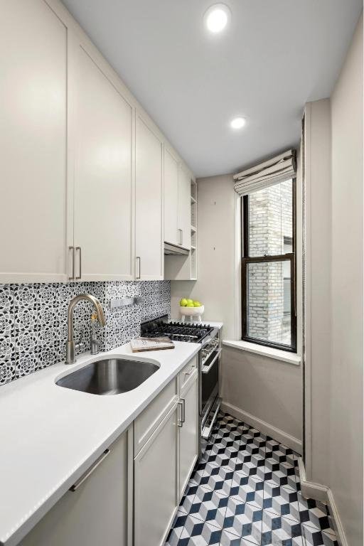 kitchen featuring tasteful backsplash, sink, gas range, and white cabinetry