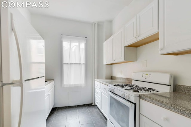 kitchen featuring white appliances, dark tile patterned flooring, and white cabinets