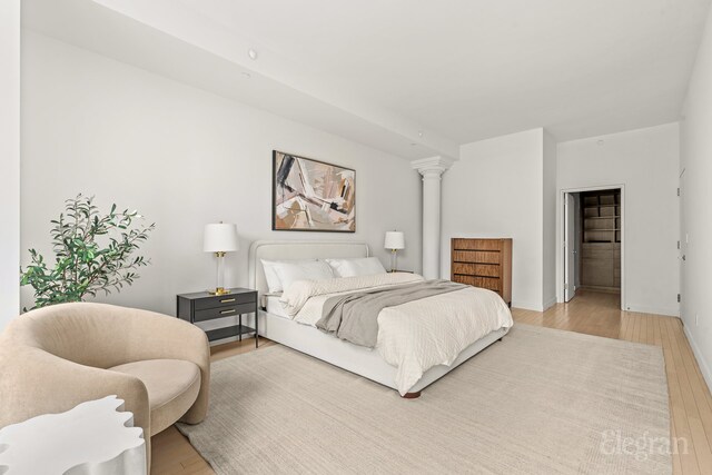 bedroom featuring ornate columns, light wood-type flooring, and baseboards