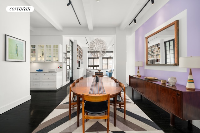 dining area with beamed ceiling, rail lighting, a chandelier, and dark wood-type flooring