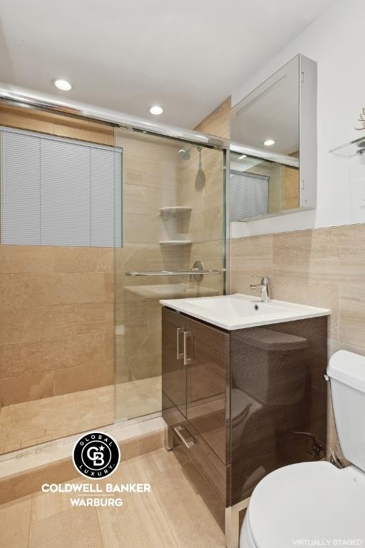 bathroom featuring tile walls, vanity, toilet, and walk in shower