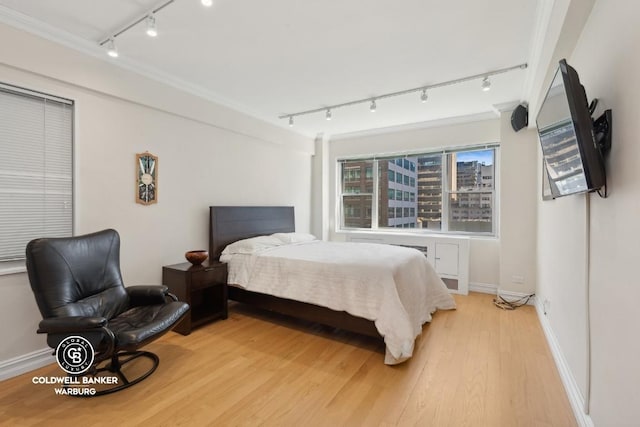 bedroom with rail lighting, ornamental molding, and light wood-type flooring