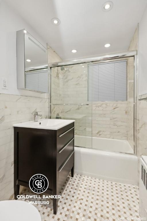 full bathroom featuring toilet, tile walls, radiator heating unit, vanity, and tiled shower / bath combo