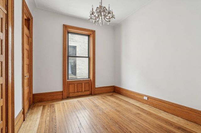 unfurnished room featuring light wood-type flooring, an inviting chandelier, and baseboards