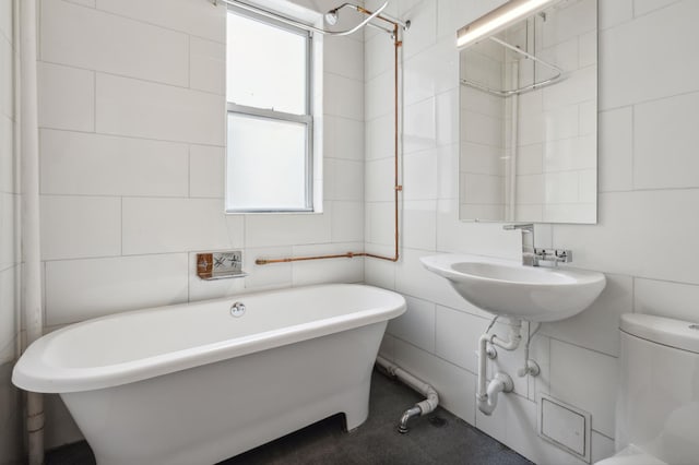 bathroom featuring a sink, a freestanding bath, tile walls, and toilet