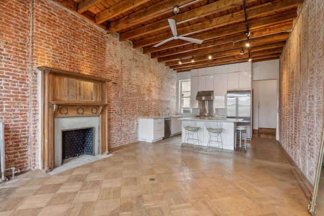 unfurnished living room featuring brick wall, a high ceiling, a fireplace, and wood ceiling