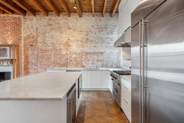 kitchen featuring beam ceiling, white cabinets, modern cabinets, high quality appliances, and under cabinet range hood