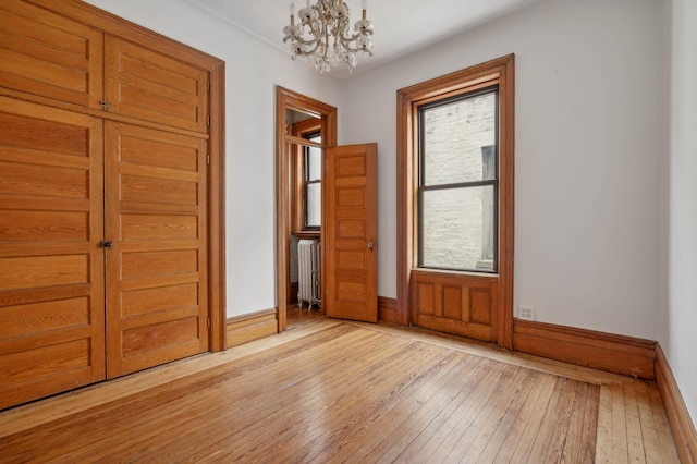 unfurnished bedroom with a chandelier, baseboards, light wood finished floors, and radiator heating unit