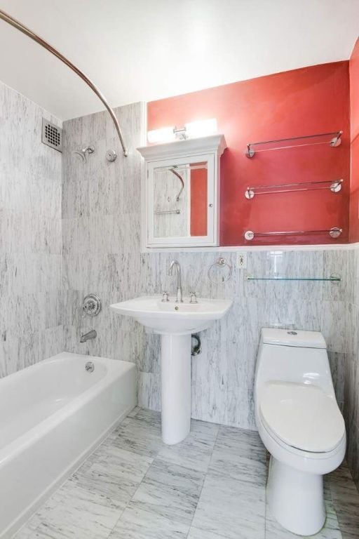 bathroom featuring toilet, tile walls, and tiled shower / bath