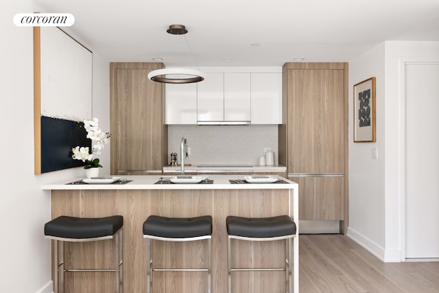 kitchen with white cabinetry, backsplash, a kitchen breakfast bar, kitchen peninsula, and light hardwood / wood-style flooring