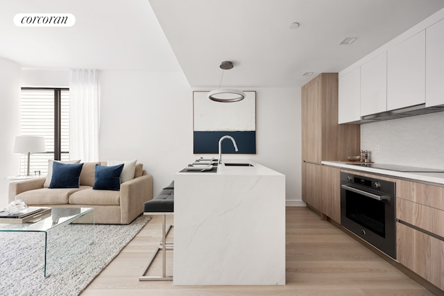 kitchen with decorative light fixtures, white cabinetry, an island with sink, black electric stovetop, and stainless steel oven