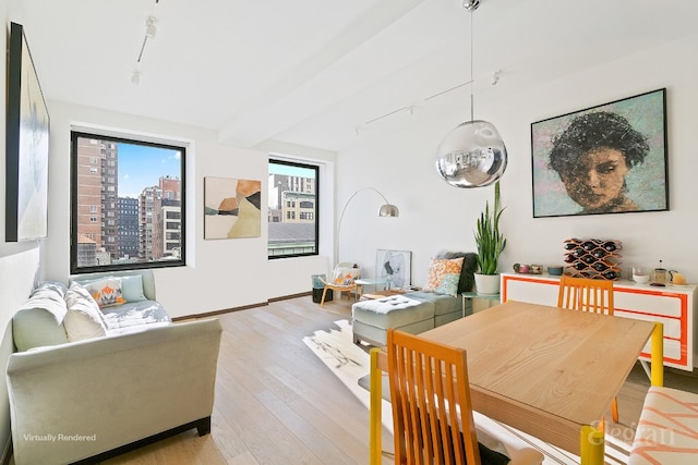 dining area featuring rail lighting, beam ceiling, and light hardwood / wood-style flooring