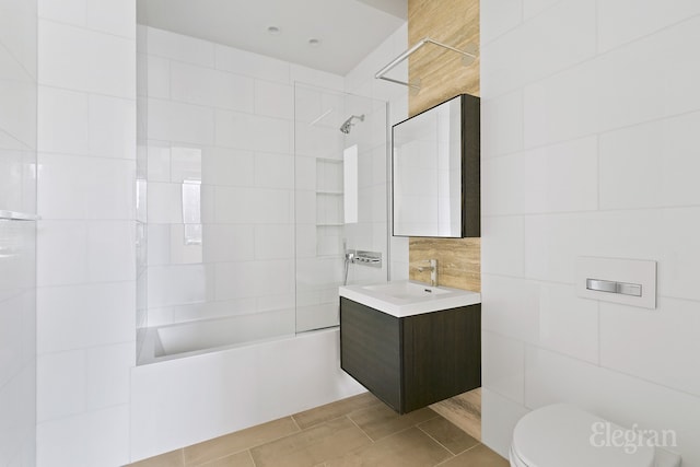 full bath featuring toilet, tile patterned floors,  shower combination, vanity, and tile walls