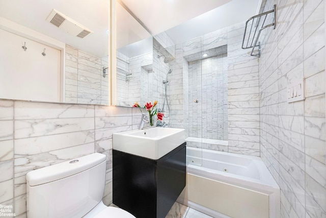 full bathroom with tile walls, toilet, vanity, and tiled shower / bath