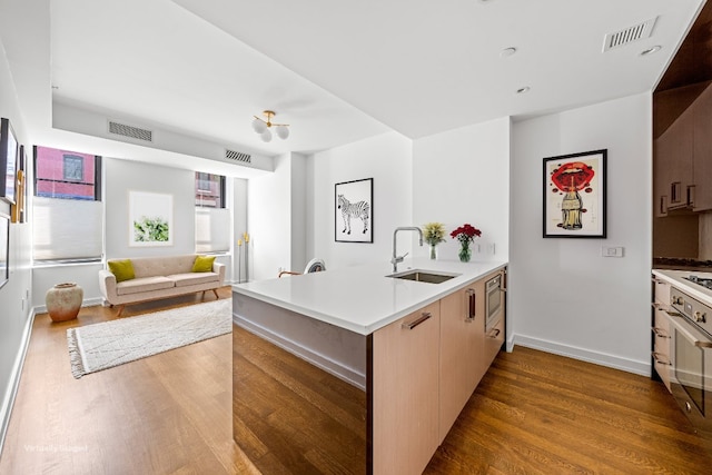 kitchen with hardwood / wood-style flooring, sink, light brown cabinets, and kitchen peninsula