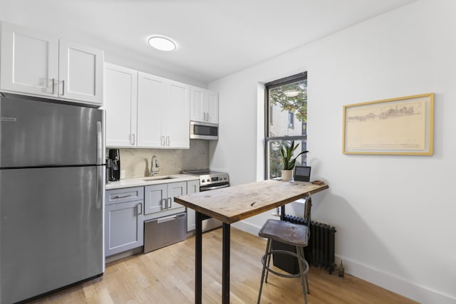 kitchen with stainless steel appliances, light countertops, light wood-style flooring, white cabinets, and a sink