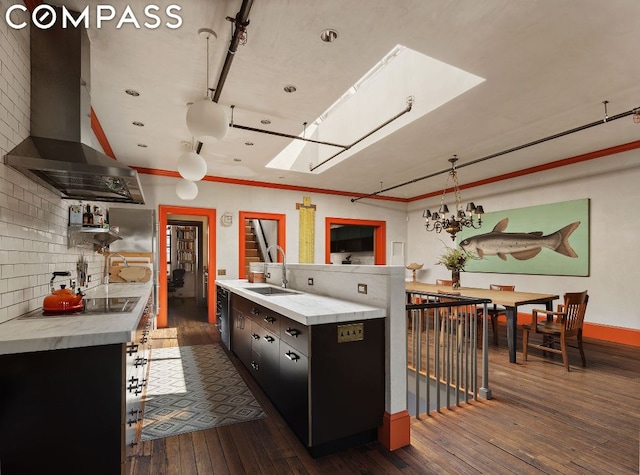 kitchen featuring backsplash, wall chimney range hood, sink, a skylight, and black electric cooktop