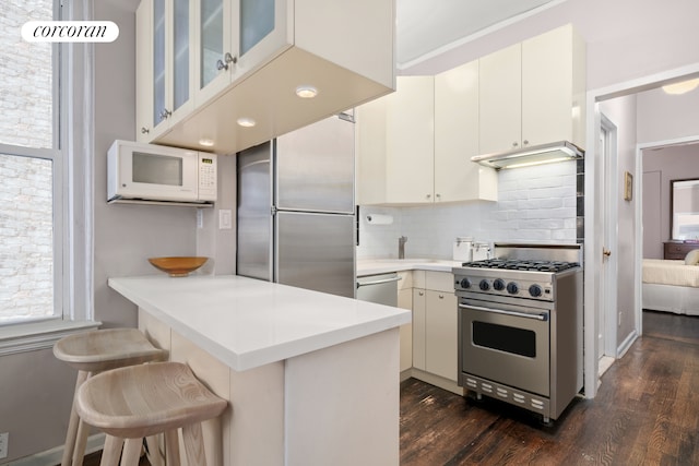 kitchen with tasteful backsplash, glass insert cabinets, light countertops, appliances with stainless steel finishes, and a peninsula