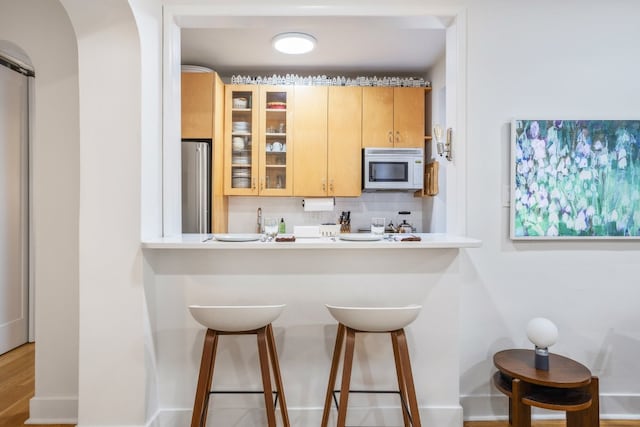 kitchen with a kitchen bar, stainless steel fridge, light brown cabinetry, and decorative backsplash