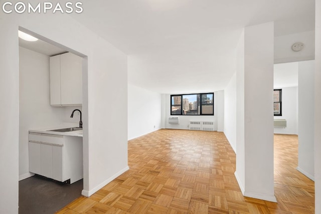 unfurnished living room featuring light parquet flooring, sink, and radiator heating unit