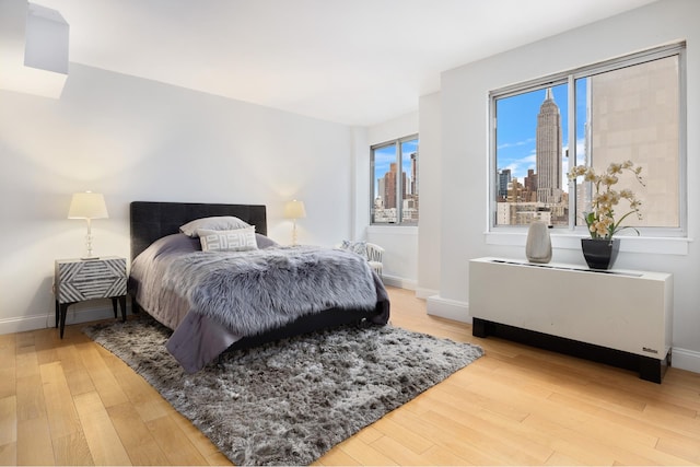 bedroom with a view of city, light wood-style flooring, and baseboards