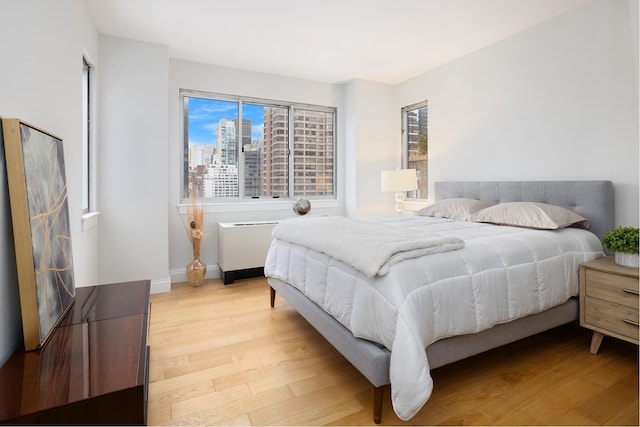 bedroom featuring a view of city, light wood-style flooring, and baseboards