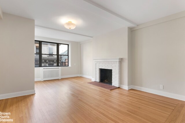 unfurnished living room featuring a brick fireplace, wood-type flooring, and radiator heating unit