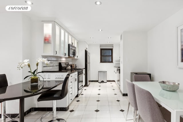 kitchen with white cabinets, decorative backsplash, light tile patterned flooring, and stainless steel appliances