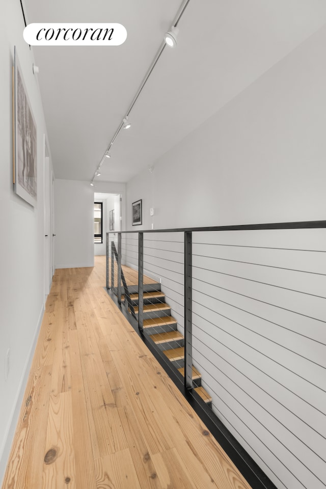 hallway with track lighting, light wood-style flooring, and an upstairs landing