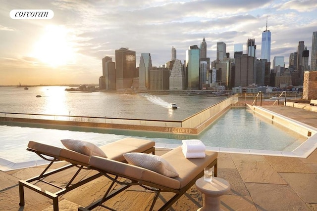 pool at dusk featuring a patio and a water view