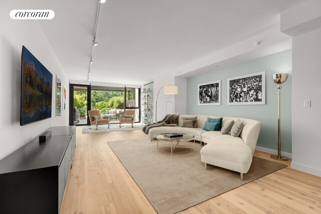 living area featuring visible vents, track lighting, baseboards, a wall of windows, and light wood-type flooring
