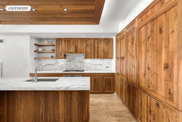 kitchen with stainless steel gas cooktop, light hardwood / wood-style floors, sink, tasteful backsplash, and a raised ceiling