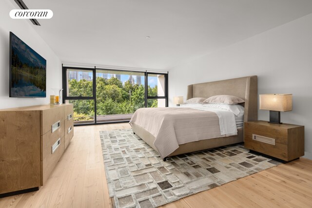 bedroom featuring light wood-style flooring, access to exterior, and a wall of windows