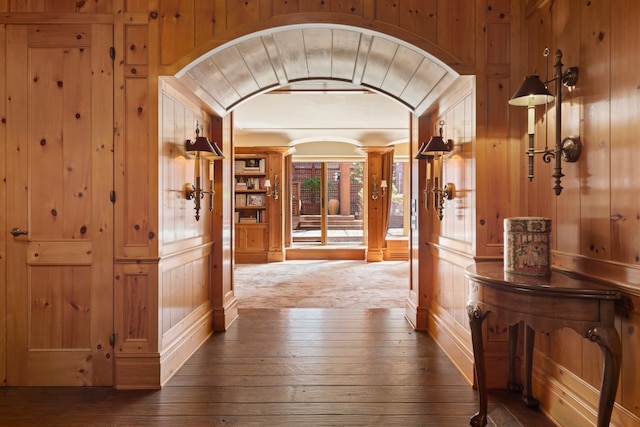 hallway featuring arched walkways, vaulted ceiling, wood walls, and hardwood / wood-style floors