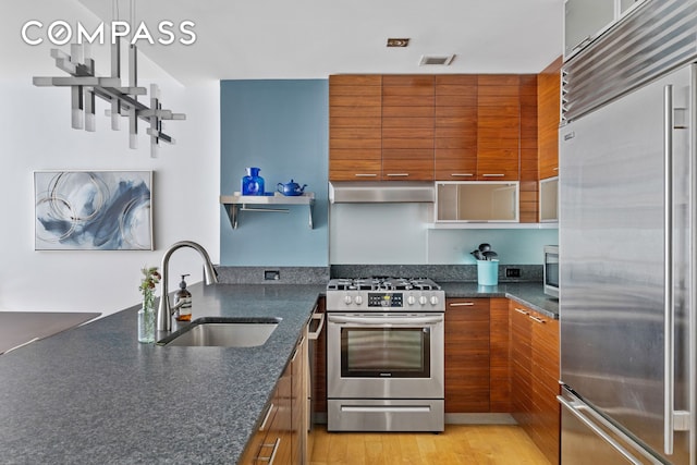 kitchen featuring modern cabinets, appliances with stainless steel finishes, brown cabinets, under cabinet range hood, and a sink