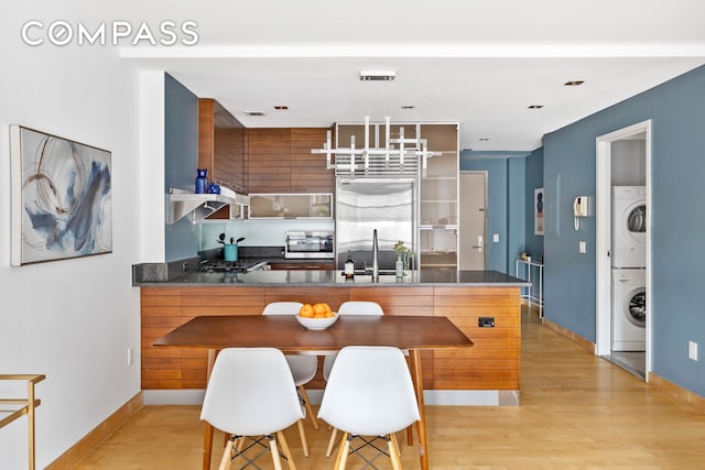 kitchen with stacked washer and clothes dryer, a peninsula, light wood-style floors, a sink, and built in fridge